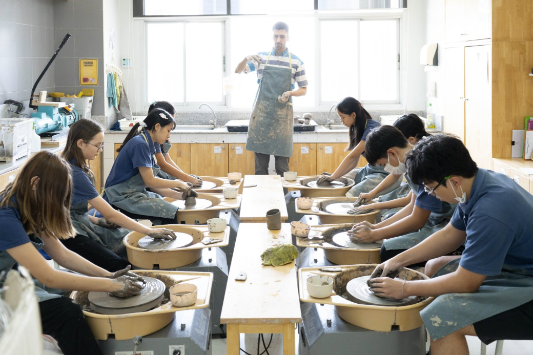 Students participating in a supervised pottery class using ceramic wheels.