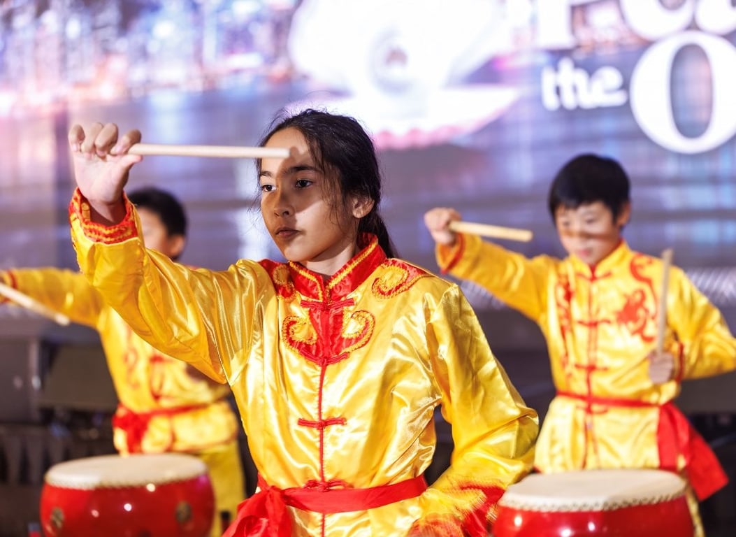 Students performing a traditional Chinese drumming routine on stage.