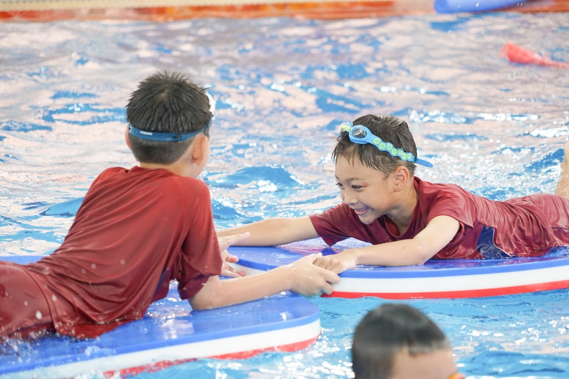 Students practice teamwork with kickboards during a swimming lesson.