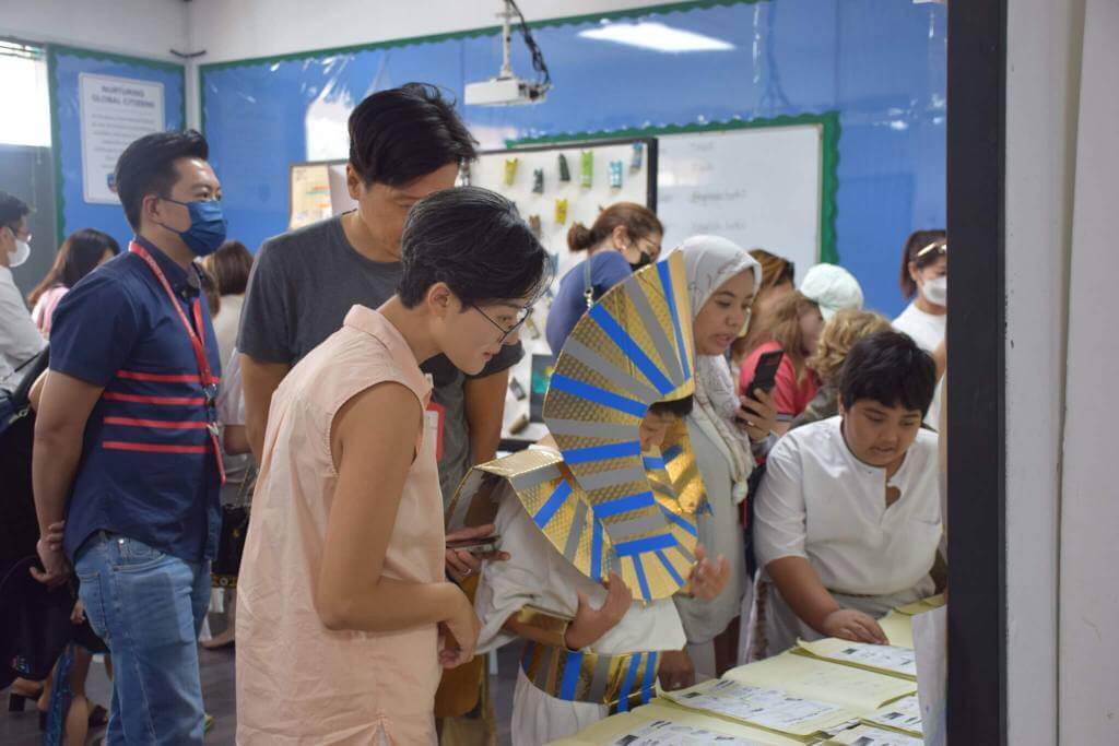 Parents and students engage in a themed classroom showcase, with learners dressed in historical costumes and presenting their projects.