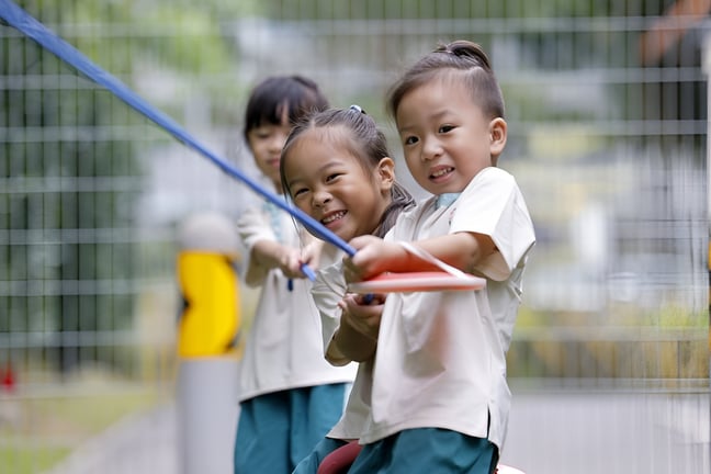 Children smiling and working together in a fun outdoor tug-of-war activity.