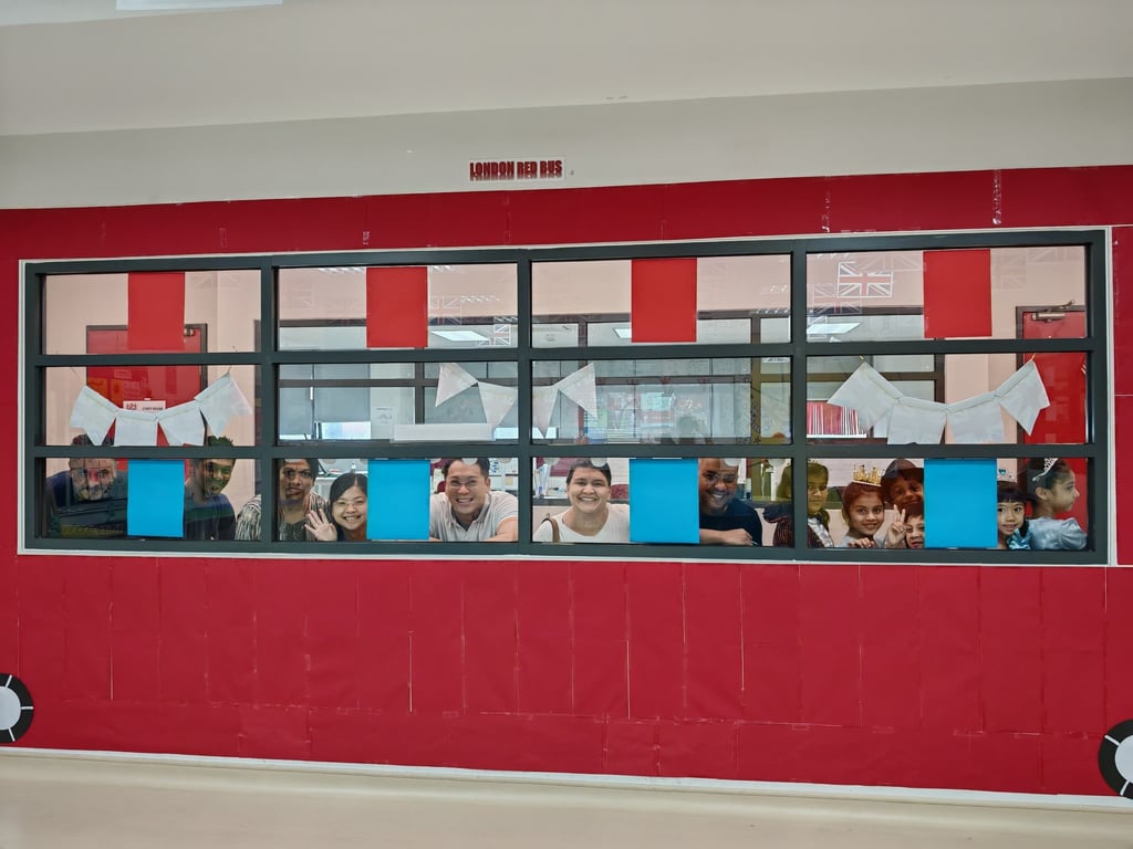 Students and parents seated together behind a decorated classroom window display.