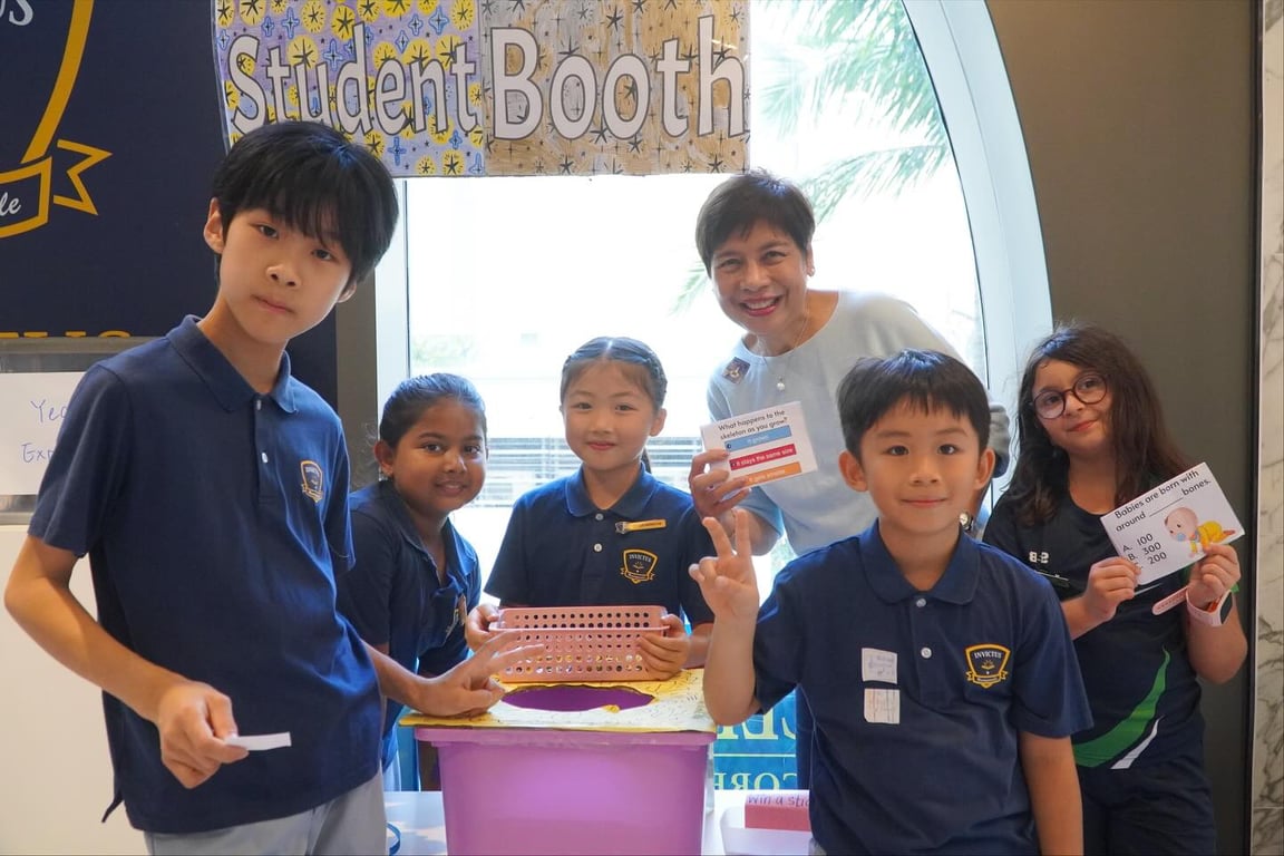 Primary students and a teacher running a trivia game at the student booth.