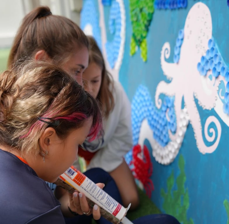 Children adding details to a marine mural using plastic caps.