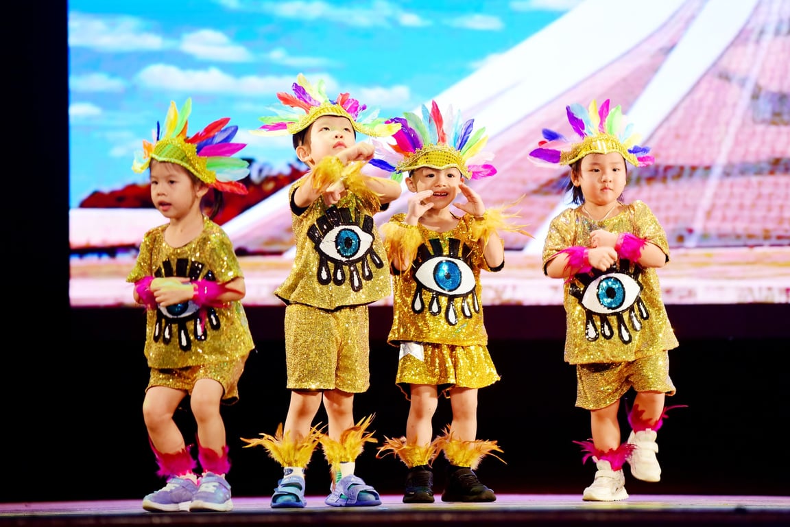 Children performing on stage in gold costumes with feathered headpieces.