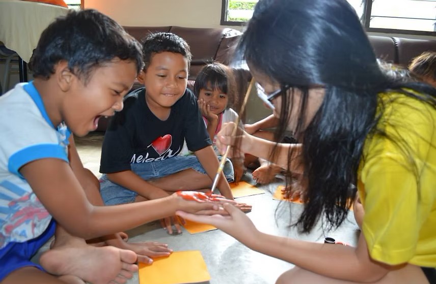 Oakrich student volunteers lead a fun hand-painting activity with local children during a school-led social engagement trip.