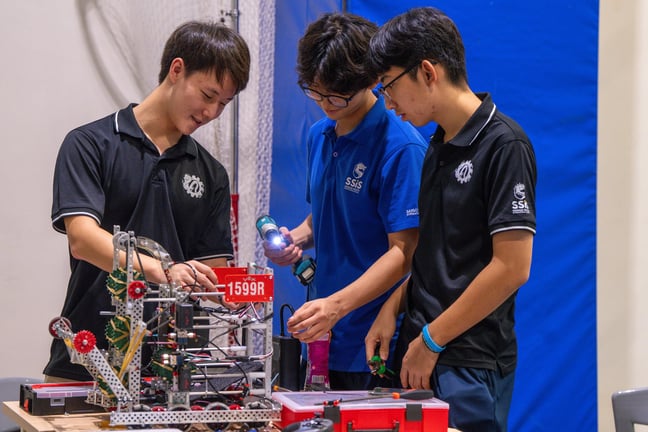 High school students collaborating on building and programming their VEX robotics project.