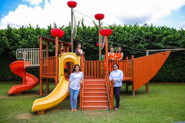 Students and teachers posing for a photo in the outdoor playground, on the climbing apparatus