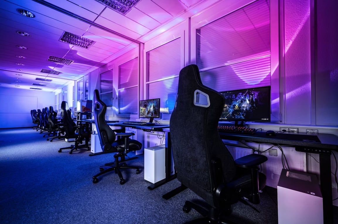 Foto de uma sala equipada com computadores, monitores, luzes led e cadeiras gamers.