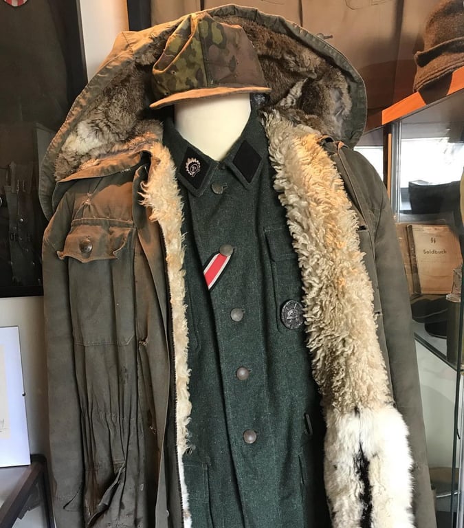 Historische deutsche Militäruniform aus dem Zweiten Weltkrieg mit einem wollenen Mantel und einer Tarnmütze, präsentiert für Sammler und Bewertungen.