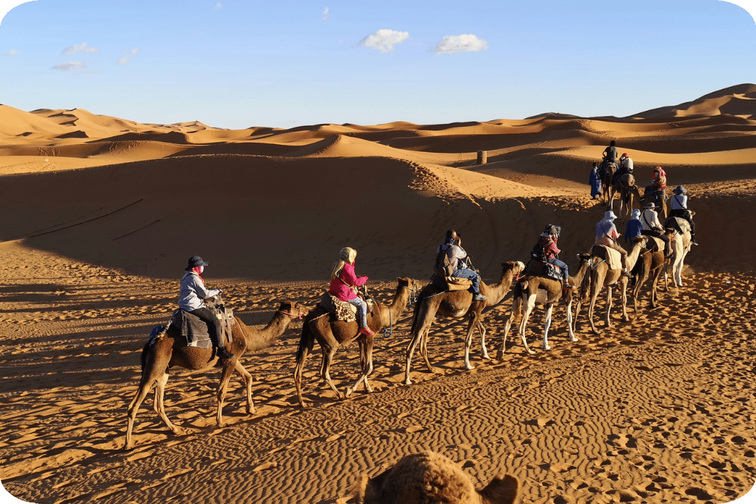A group of people riding camels through sand dunes in the dessert.