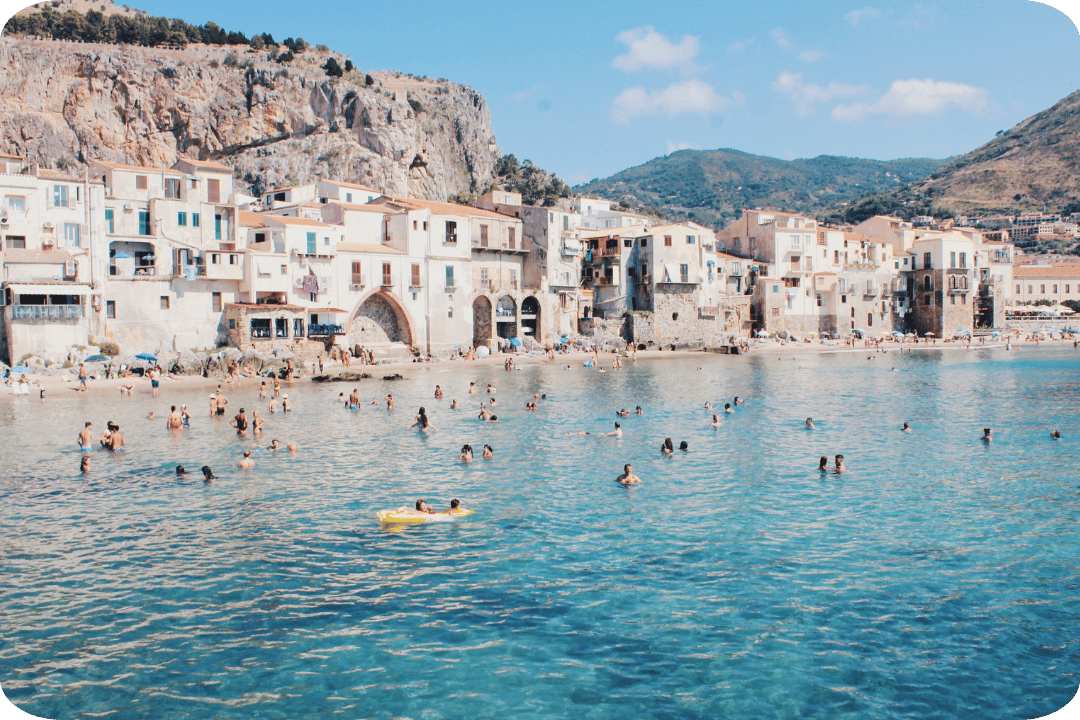 People swimming in Italy, with lovely traditional architecture and a mountainious landscape in the background.