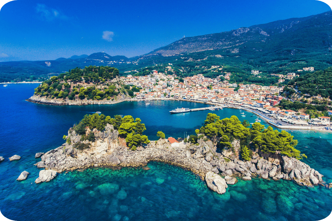 An image of Greece coast, with blue sea, houses, and a mountanious landscape.