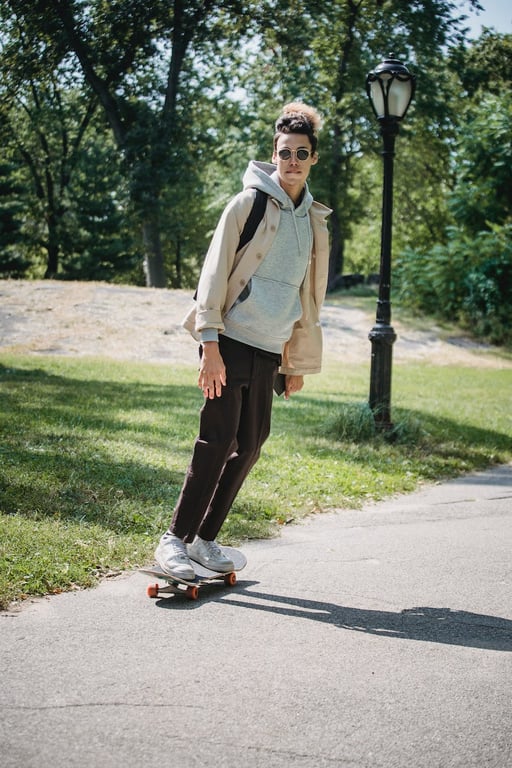 Full body of young male student in eyewear riding skateboarding along path in university campus
