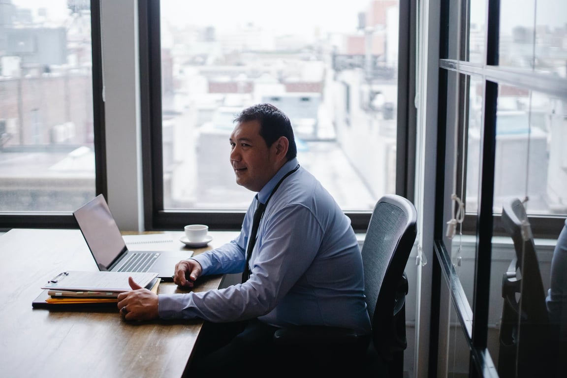 Vue latérale en plongée d'un homme d'affaires ethnique souriant assis dans un fauteuil à une table avec un ordinateur portable et des documents.