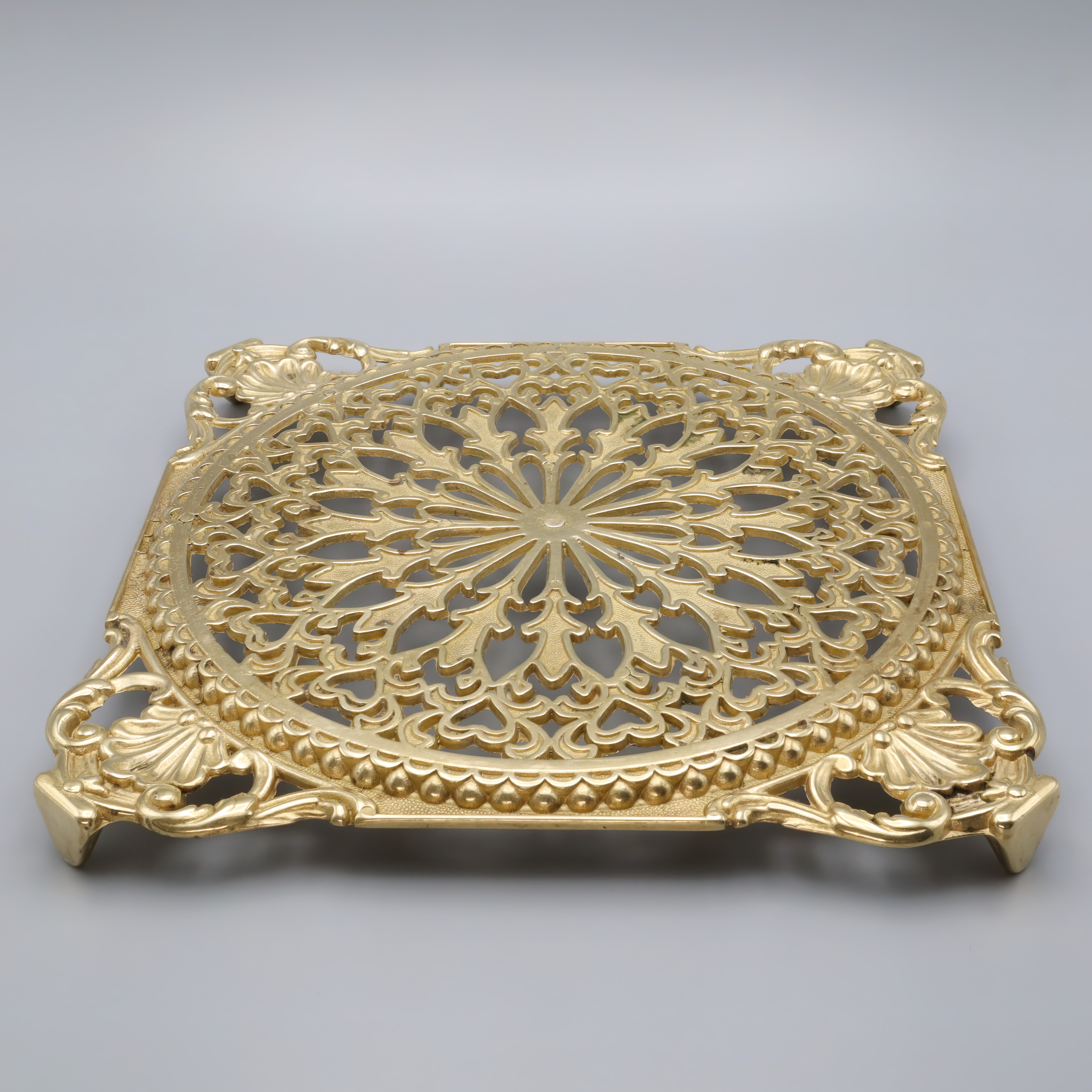 Antique brass trivet with intricate floral pattern and ornate detailing, close up view for vintage kitchen decor and cookware