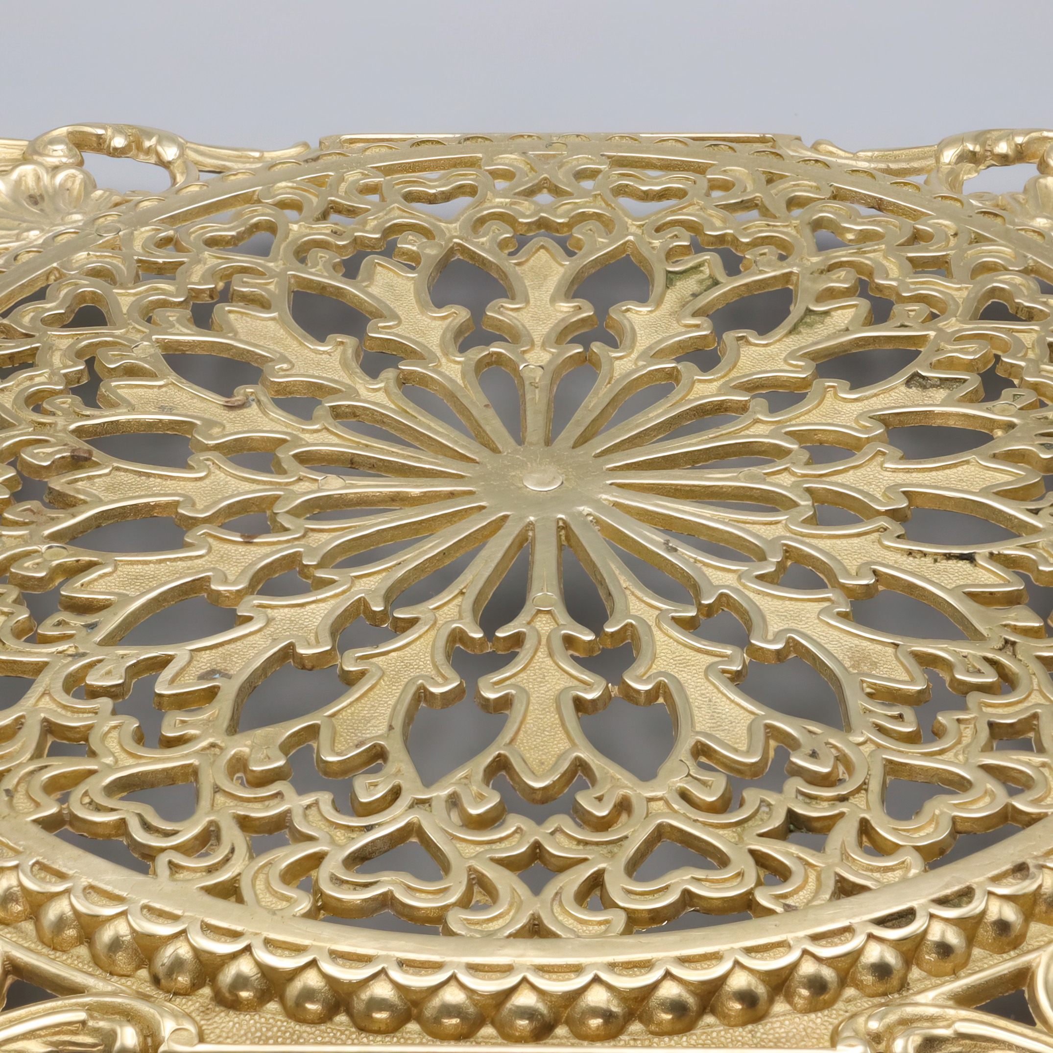 Antique brass trivet detailed view showing ornate vintage metalwork and intricate decorative pattern