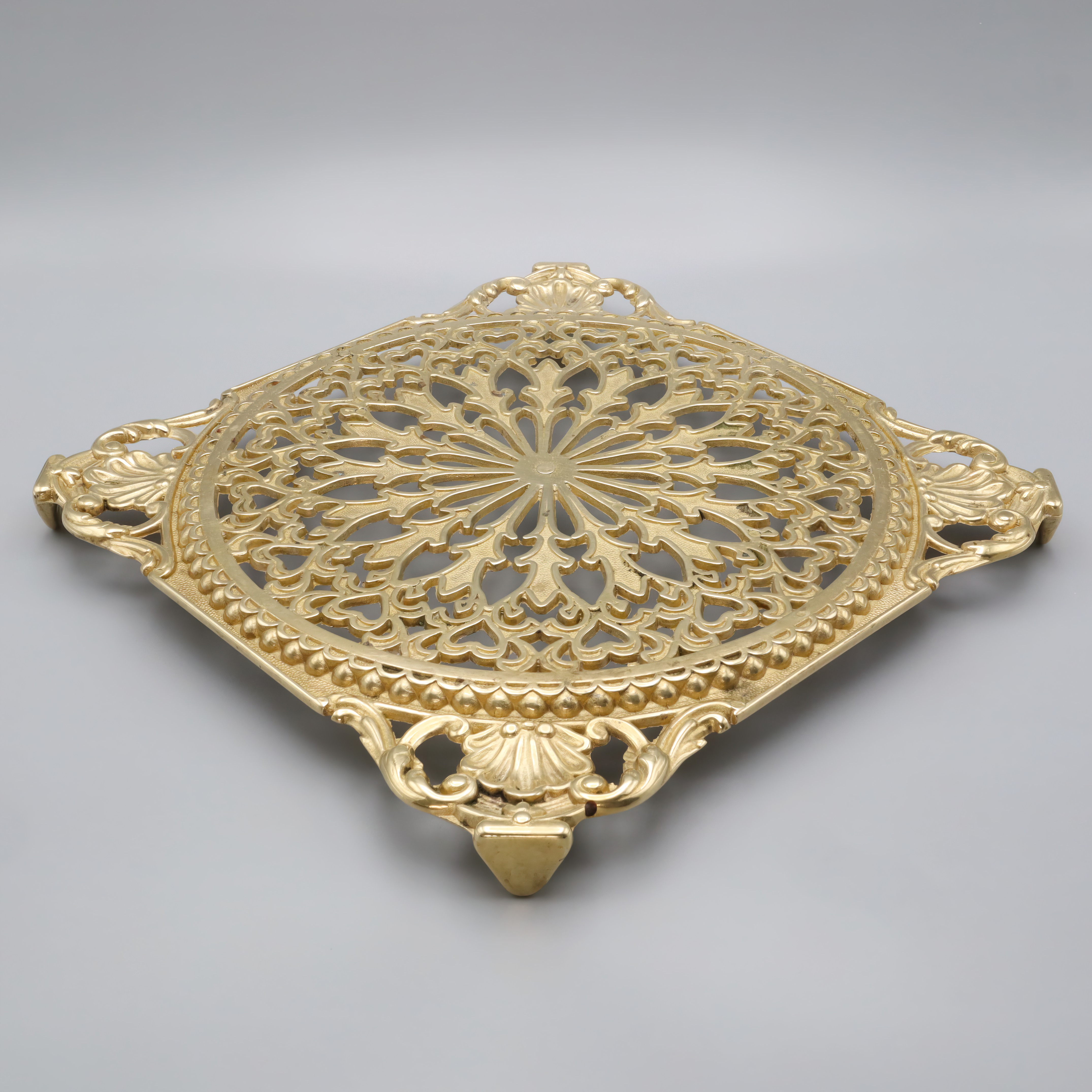 Antique brass trivet with intricate floral pattern, close up of vintage decorative kitchen accessory