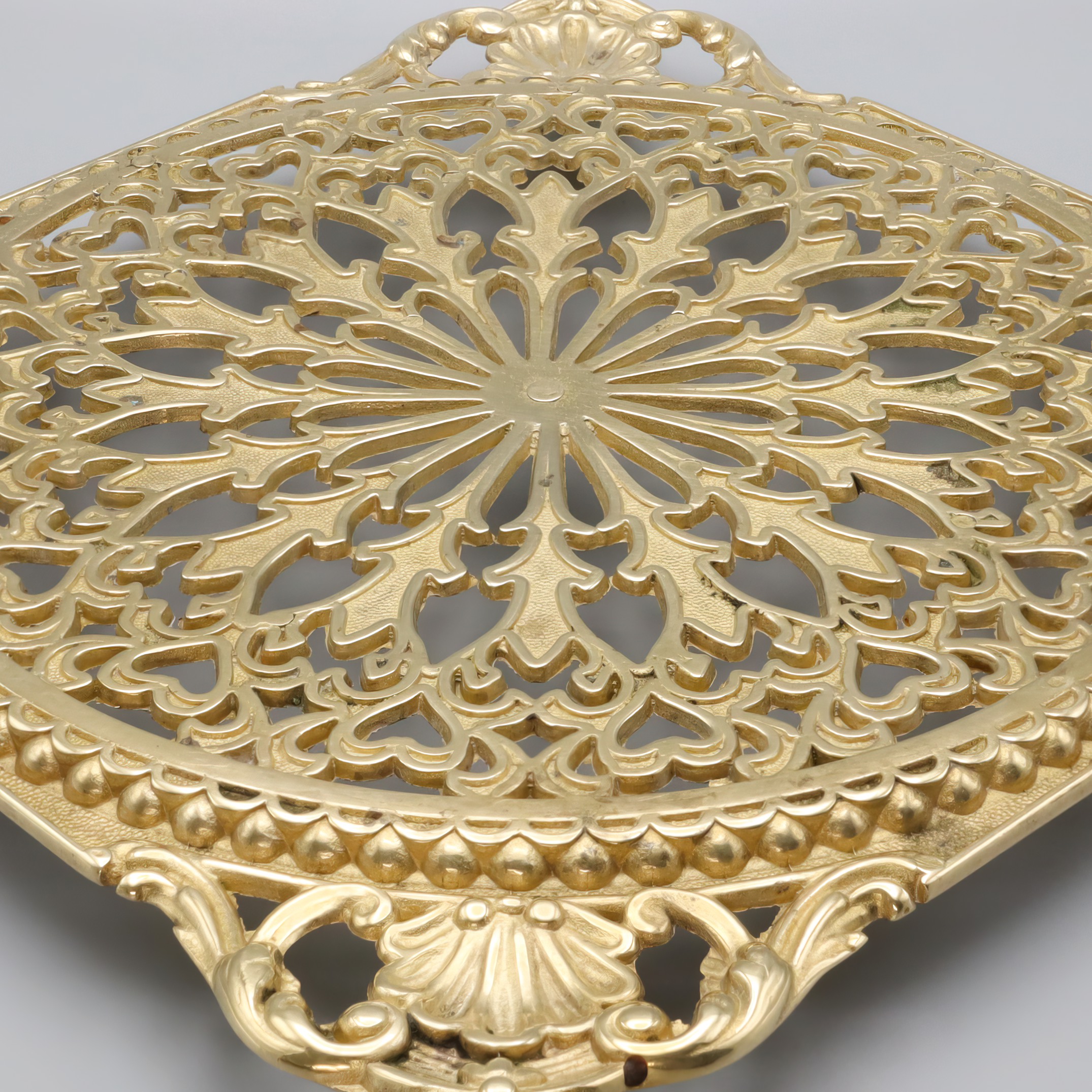 Antique brass trivet close up showing ornate vintage floral design and intricate craftsmanship