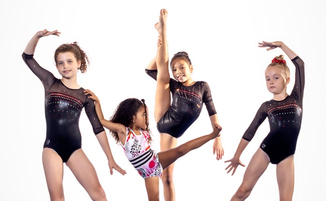 Four young gymnasts holding various gymnastics poses looking at camera