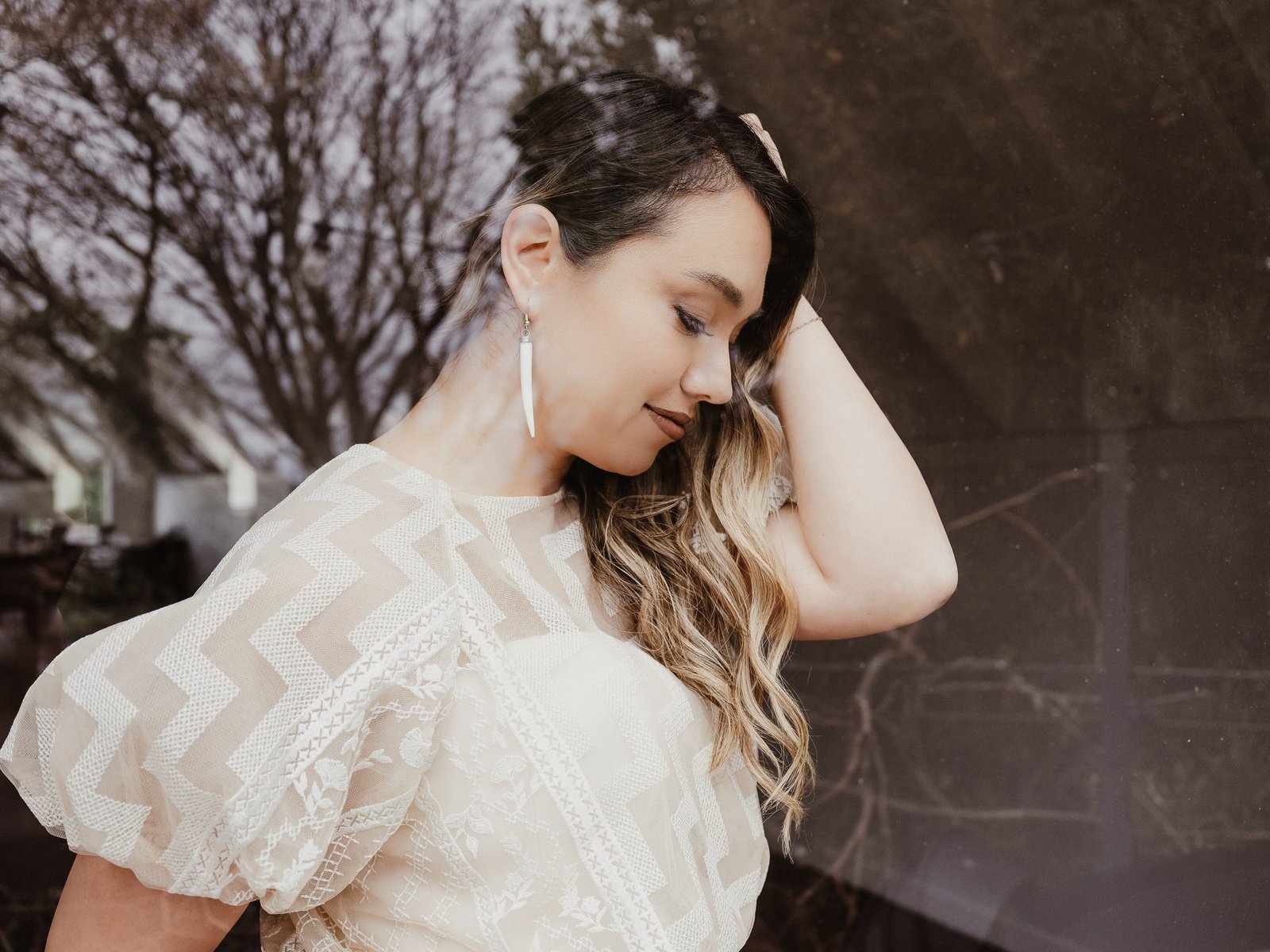 Bride in a white tukutuku lace top posing outdoors with one hand in her hair.