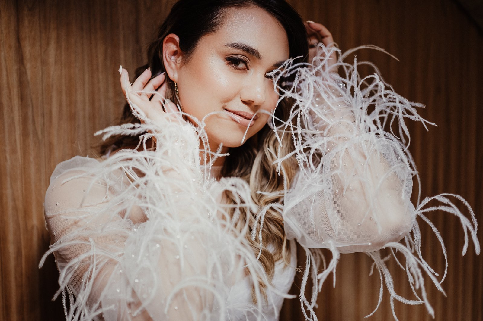 Close portrait of a bride in a white feathered gown, resting one hand against her face.