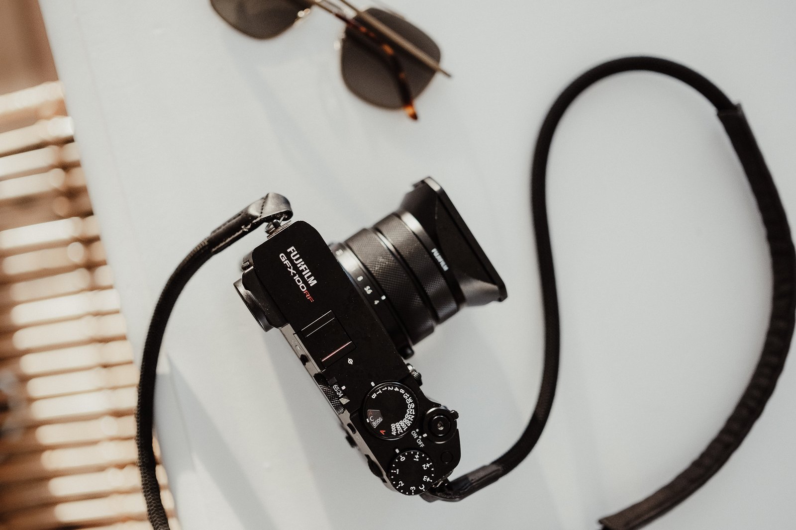 Top-down view of a Fujifilm GFX100RF camera resting on a table beside camera accessories.