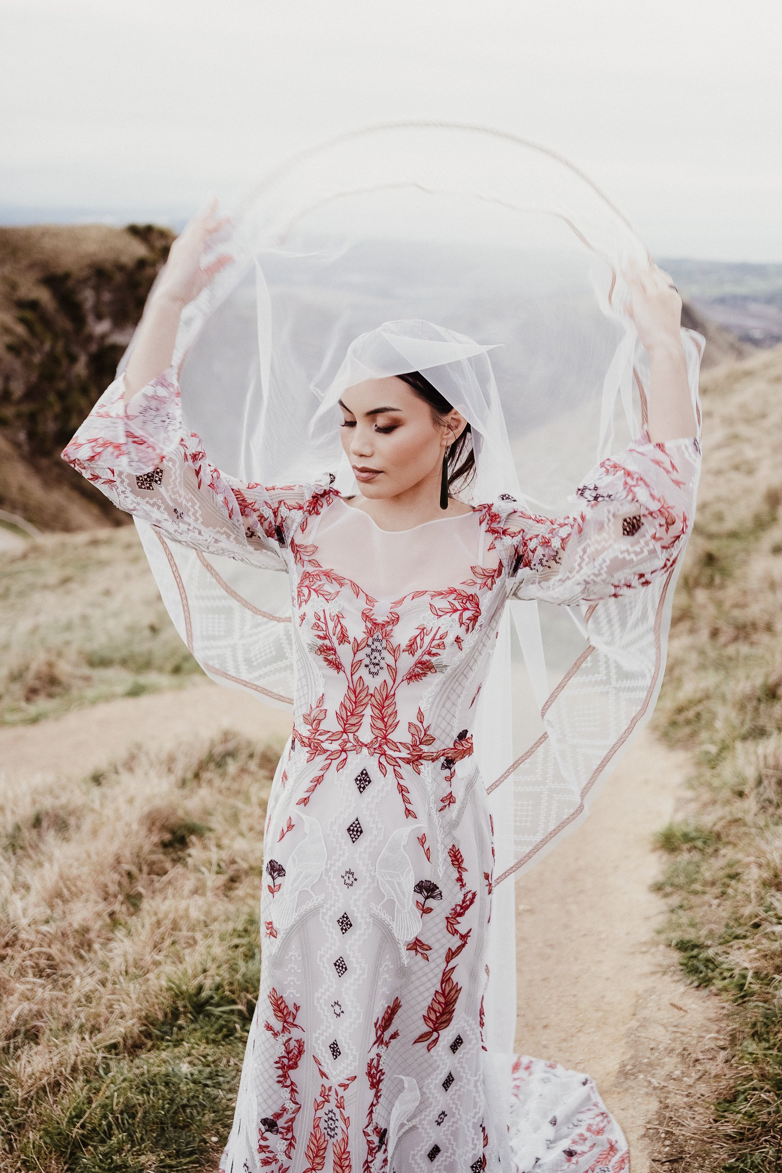 Bride in the red and white Huia gown lifting her veil above her head at Te Mata Peak.