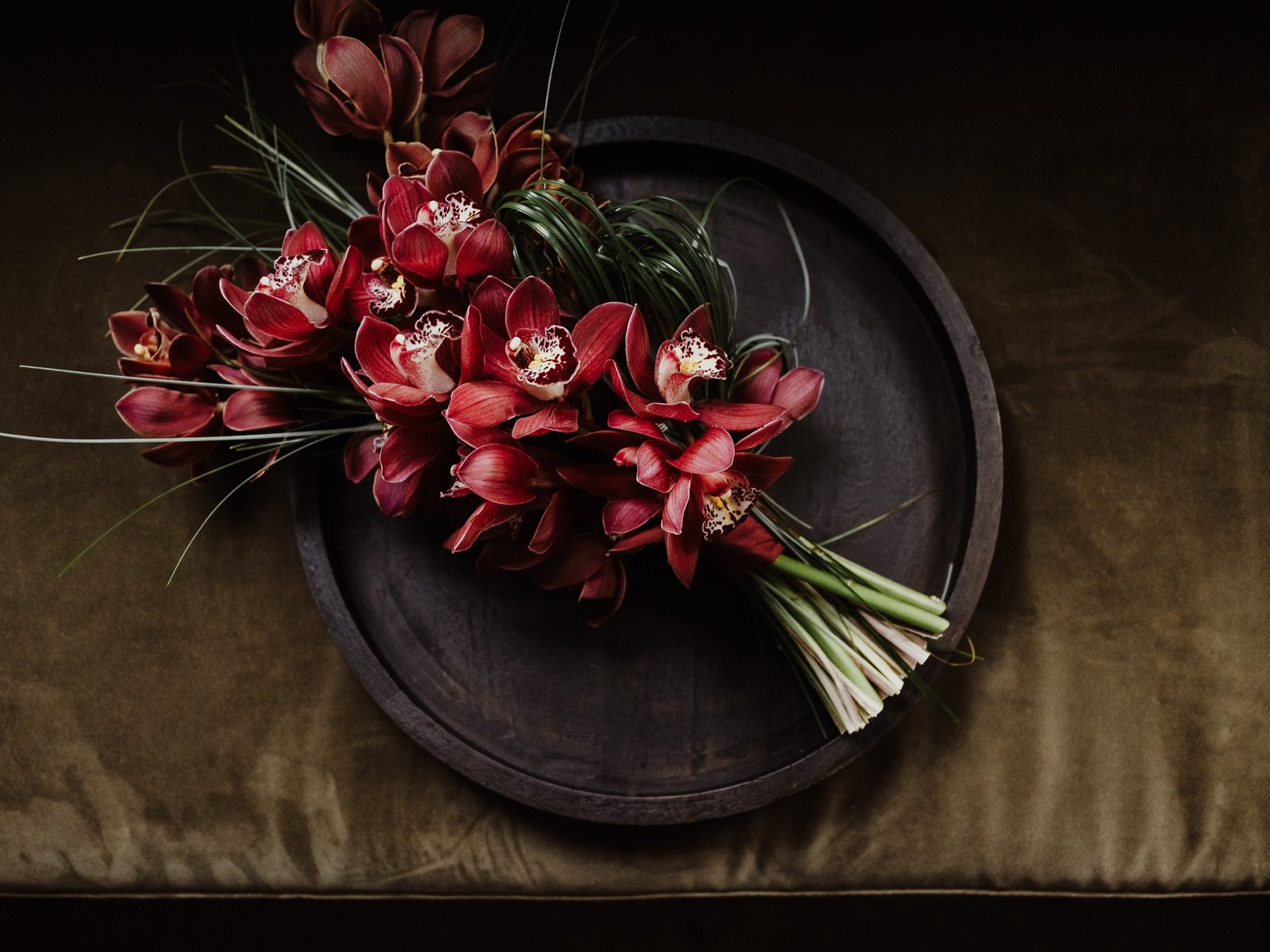 Deep red bridal bouquet resting on a dark platter against an olive-green cloth.