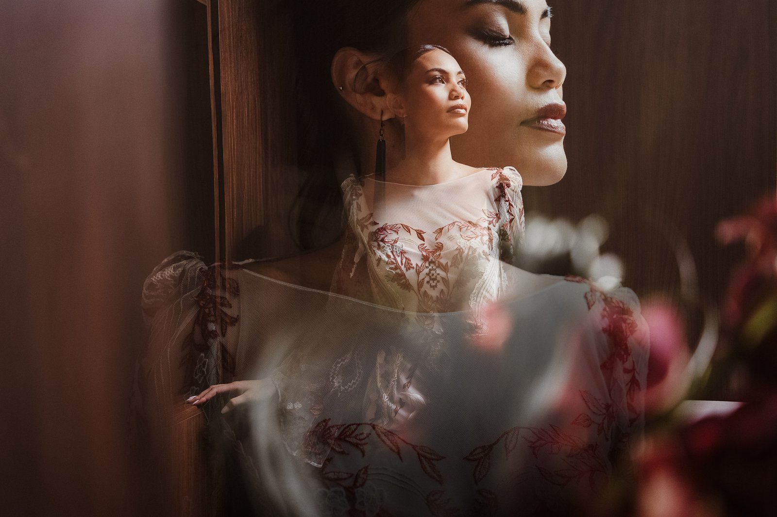 Double-exposure portrait of a bride in the red and white Huia gown, illuminated by moody window light.