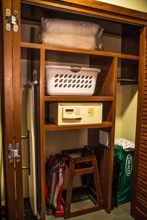 An ironing board, vaccum, high chain, crib, and safe appear inside a large closet