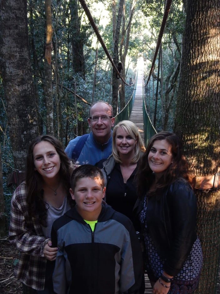 Andy Berry and family posing for a picture on a rope bridge in a forest.