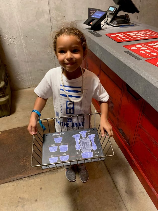 Girl holding R2-D2 droid customization tray at Galaxy's Edge Star Wars Disney Park.