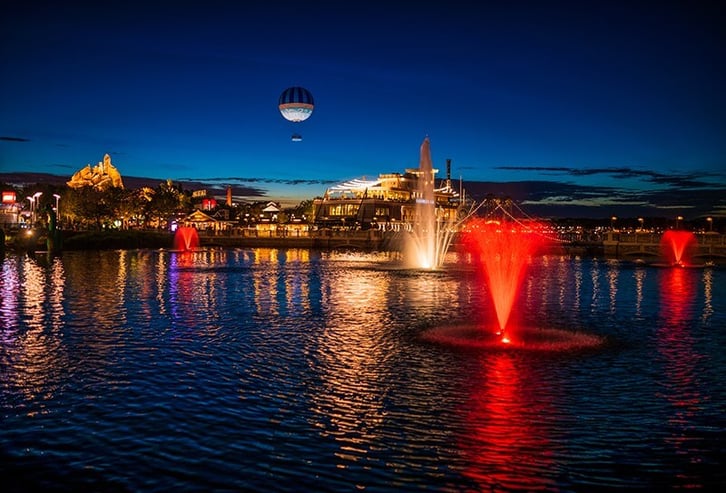 Disney Springs at night with glowing fountains of colored light and an air balloon in the sky.