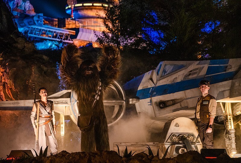 Star Wars Galaxy's Edge cast, Chewbacca, Ray, and Rebel Soldier in front of a blue X-Wing Fighter