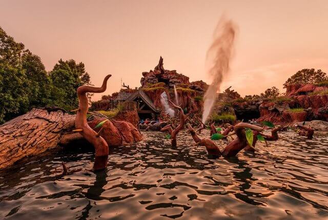 A view of splash mountain at the magic kingdom from the water with water spraying in the air.