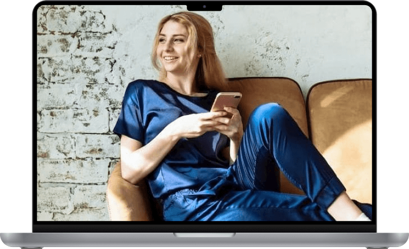 A woman holding a cellphone on a couch and smiling.
