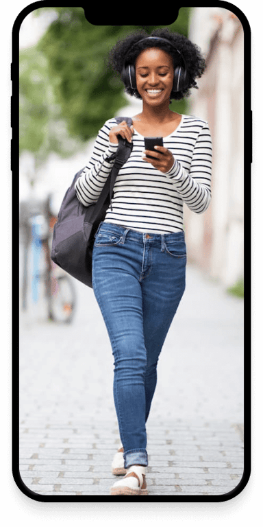 A woman holding walking down a street, smiling and looking at her phone.