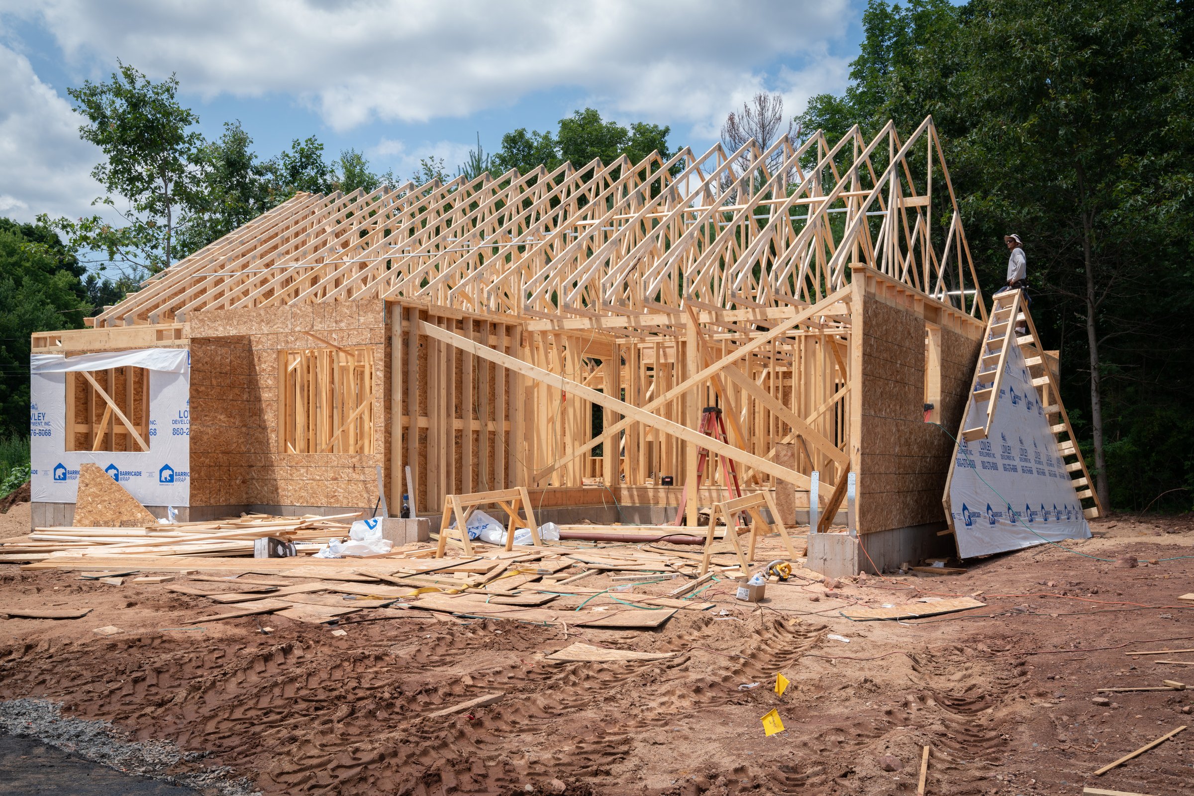 Framed house under construction with roof trusses installed and stick-framed walls below