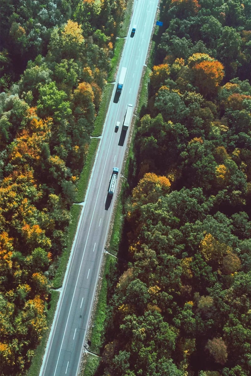 Aerial view of trucks traveling on a highway through autumn forest