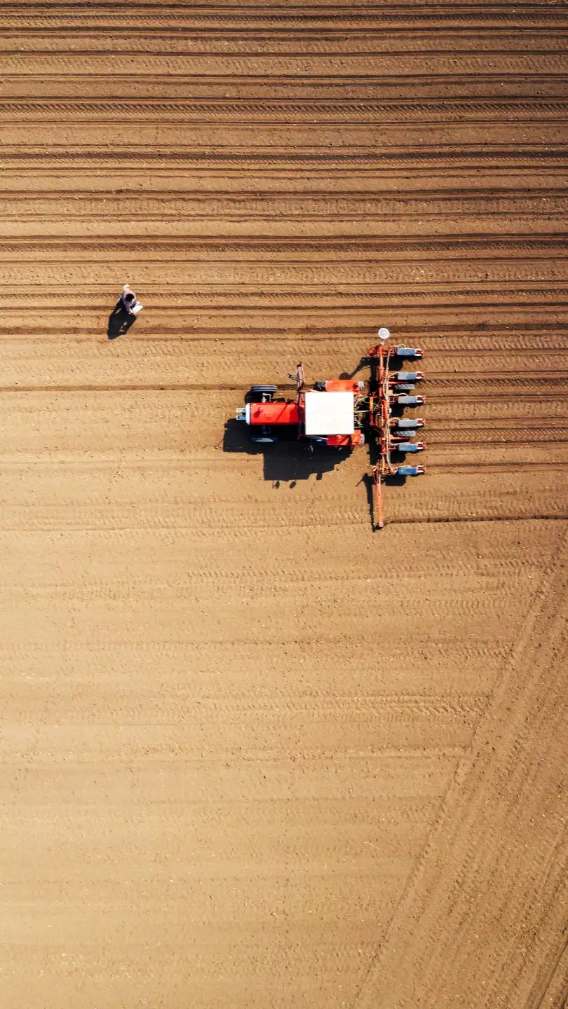Aerial view of a tractor plowing evenly spaced furrows in a field