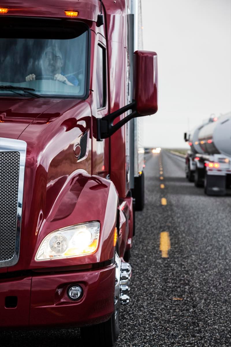 Close up view of the cab and driver of a commercial truck on the highway. Hot shot trucking - commercial truck cab driver close up