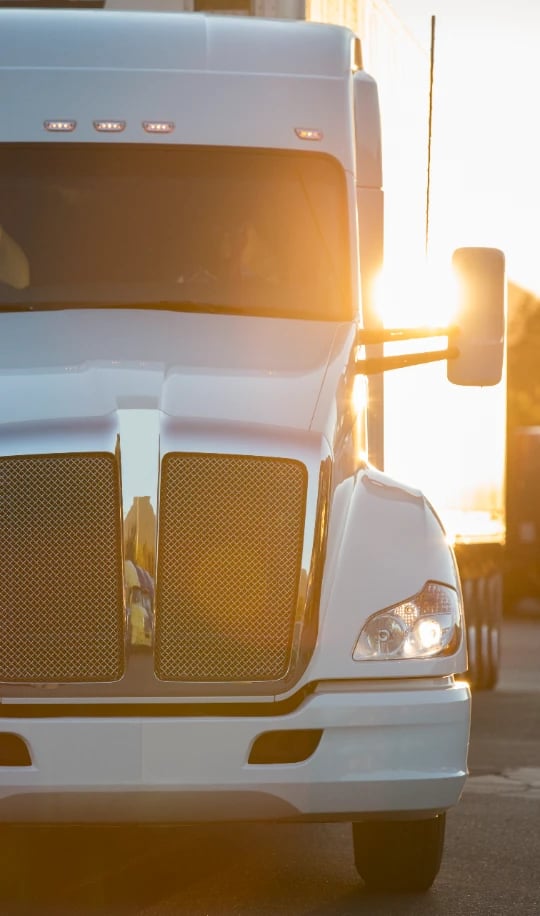 Front view of a white semi truck with sun glare behind the cab