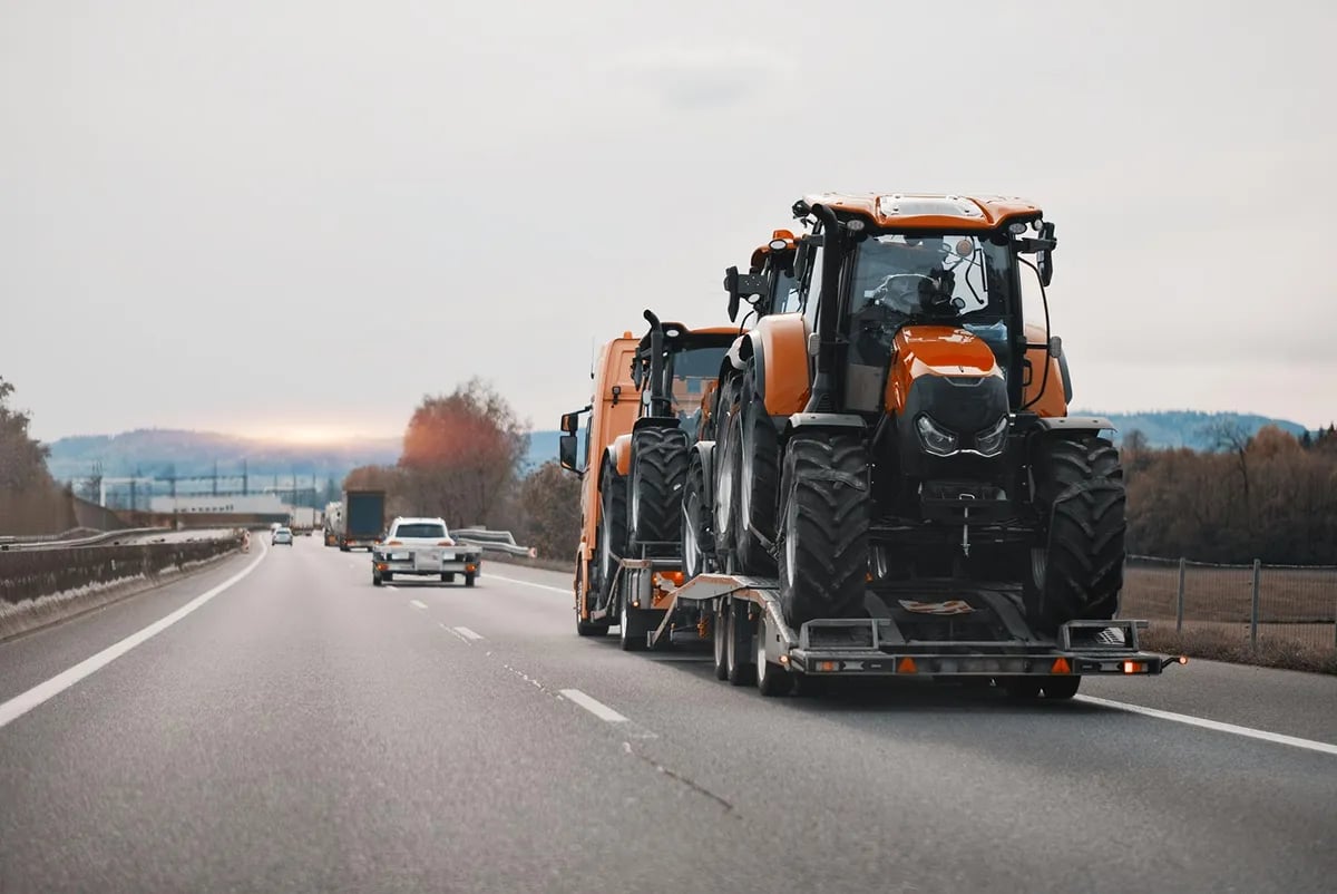 Orange agricultural tractors loaded on a transport trailer rolling down a multi-lane highway