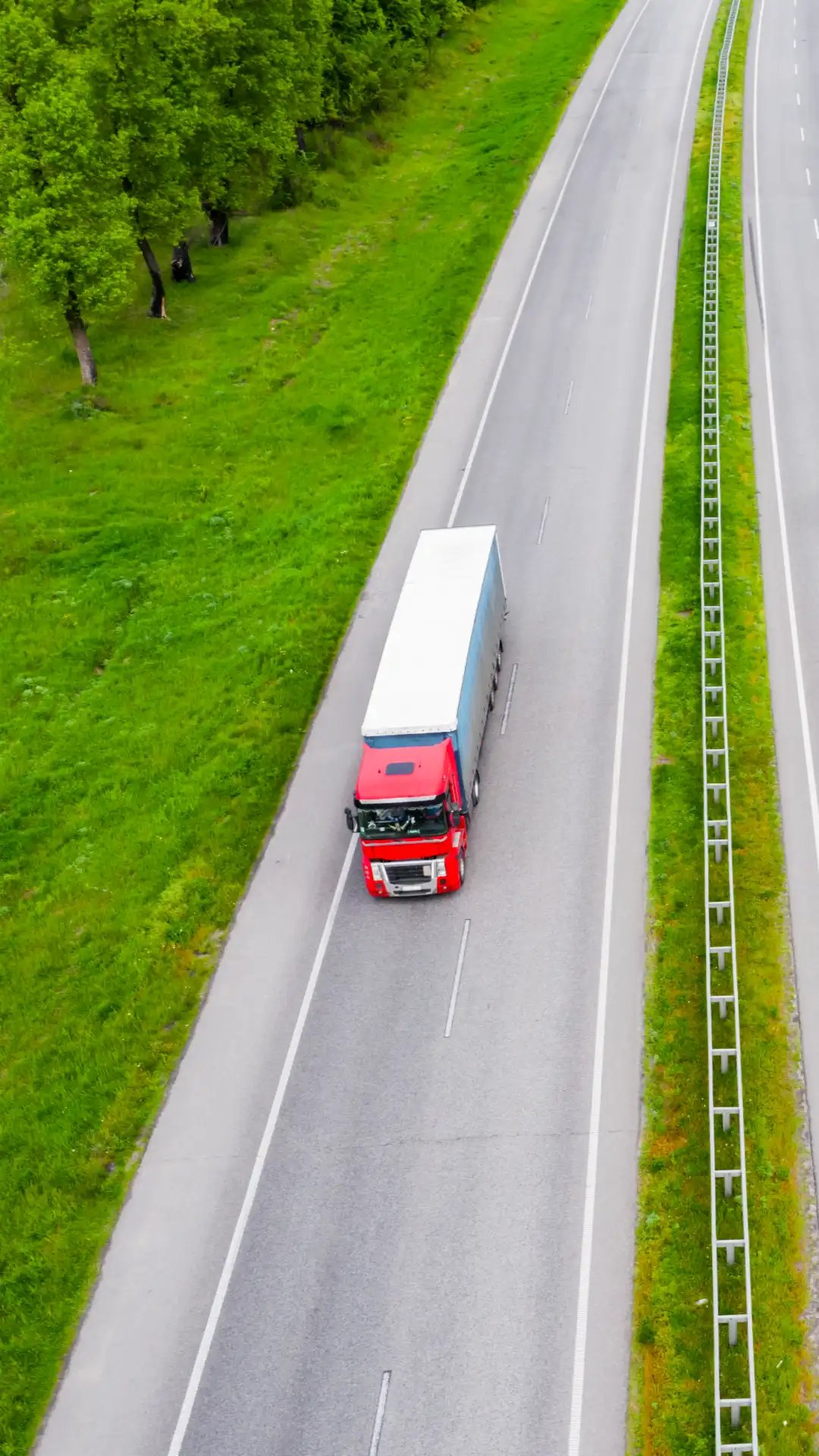 aerial-truck Red tractor-trailer driving along a green highway from an aerial view