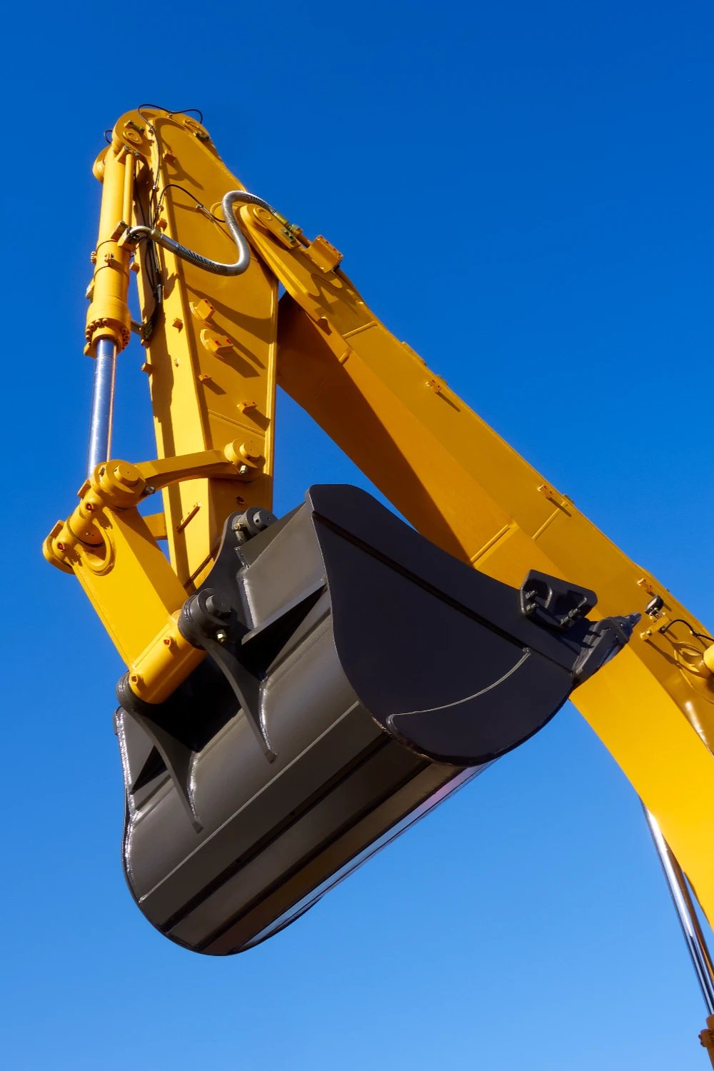 Excavator boom and bucket against a clear blue sky, the kind of tall machinery hauled on double drop trailers