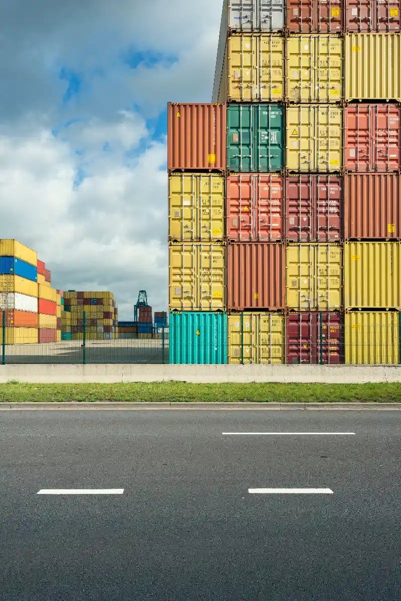 drayage3 Colourful shipping containers stacked at a port terminal beside the road, with a crane in the distance