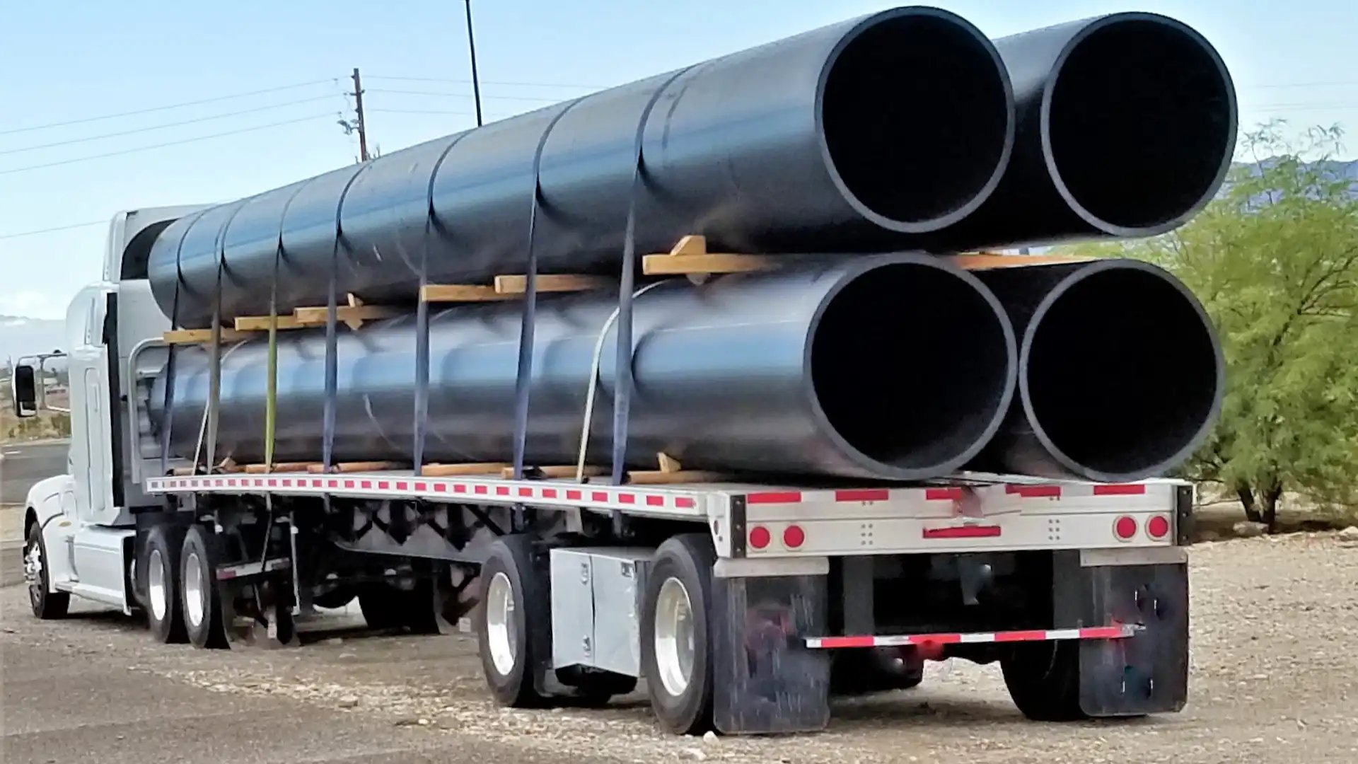 Flatbed truck carrying stacked large-diameter pipes secured by straps