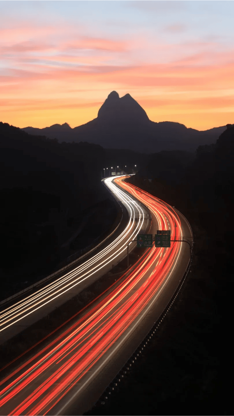fast-shipping-overnight Headlight and taillight trails streaking along a mountain highway at dusk during overnight freight runs