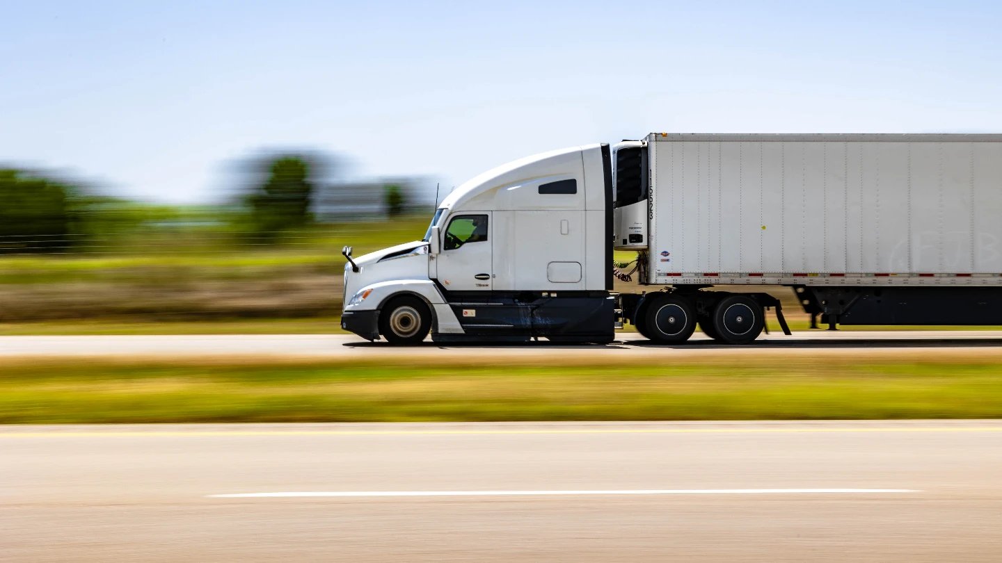 fast shipping White sleeper semi pulling a refrigerated van trailer at highway speed, scenery blurred with motion